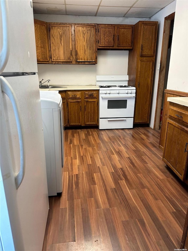 kitchen featuring a paneled ceiling, white appliances, sink, washer / clothes dryer, and dark hardwood / wood-style floors