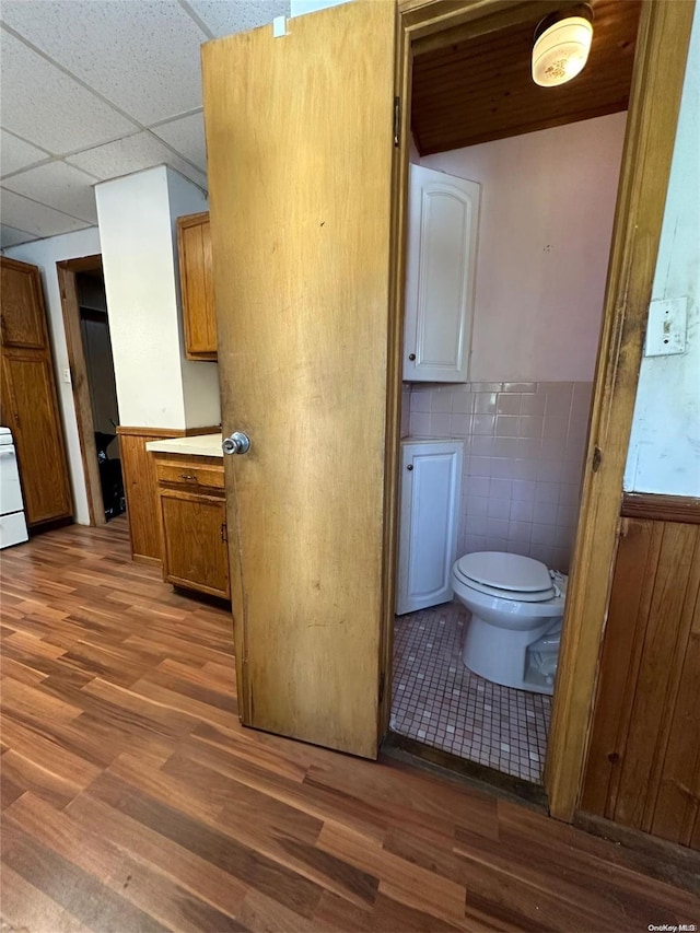 bathroom featuring a paneled ceiling, vanity, tile walls, hardwood / wood-style floors, and toilet