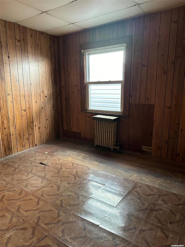 spare room featuring radiator, wood walls, and a drop ceiling