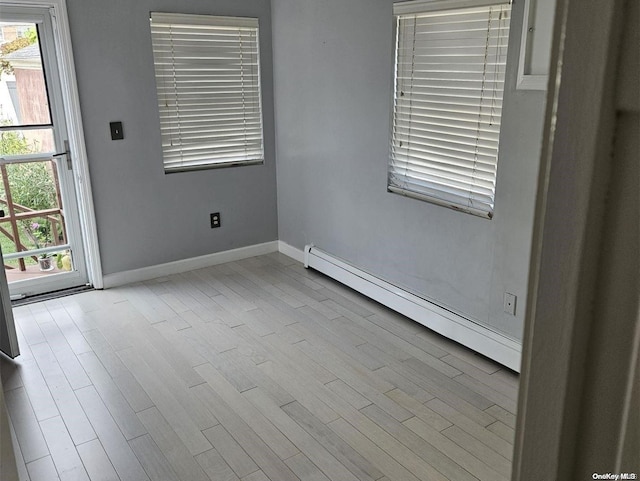 spare room featuring baseboard heating and light hardwood / wood-style flooring