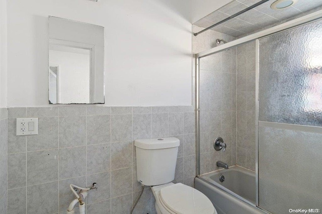 bathroom with combined bath / shower with glass door, toilet, and tile walls