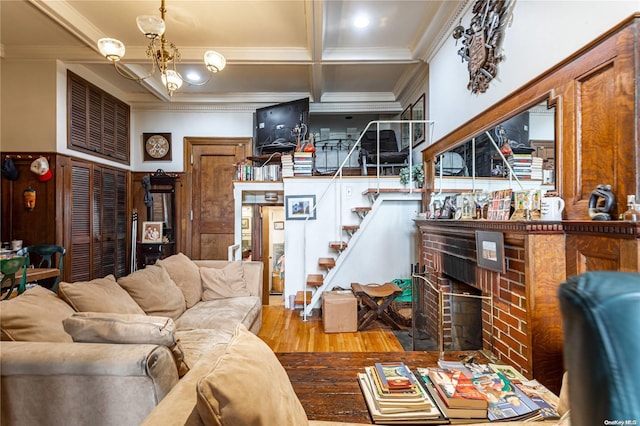 living room with a brick fireplace, crown molding, wood-type flooring, beam ceiling, and an inviting chandelier