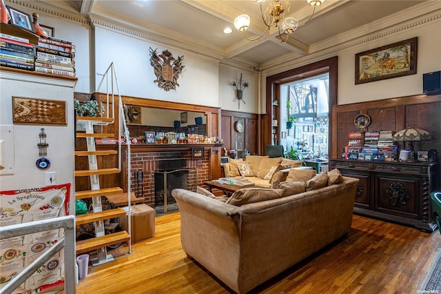 living room with coffered ceiling, ornamental molding, a fireplace, wood-type flooring, and a chandelier