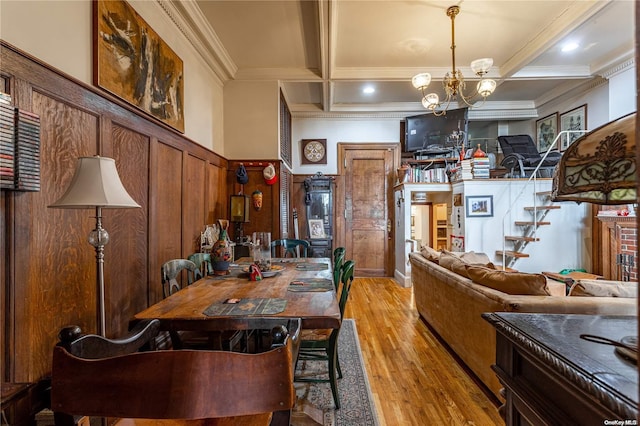 dining space featuring an inviting chandelier, crown molding, wooden walls, light wood-type flooring, and beamed ceiling