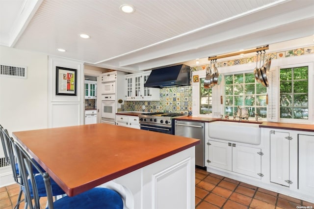 kitchen featuring sink, wall chimney exhaust hood, backsplash, white cabinets, and appliances with stainless steel finishes