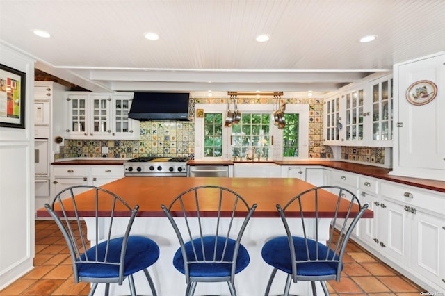 kitchen featuring white cabinets, wall chimney exhaust hood, decorative backsplash, light tile patterned flooring, and stainless steel appliances