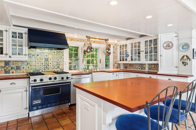 kitchen with wall chimney exhaust hood, stainless steel appliances, backsplash, a breakfast bar area, and white cabinets