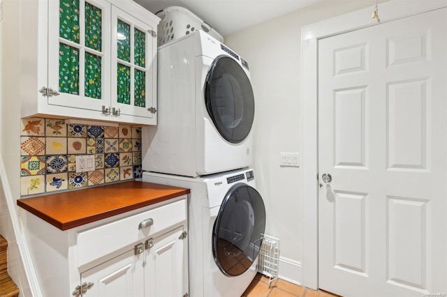 clothes washing area with cabinets, light tile patterned floors, and stacked washer / dryer