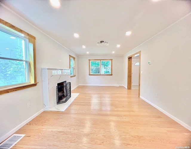 unfurnished living room with a fireplace, ornamental molding, light hardwood / wood-style flooring, and a healthy amount of sunlight