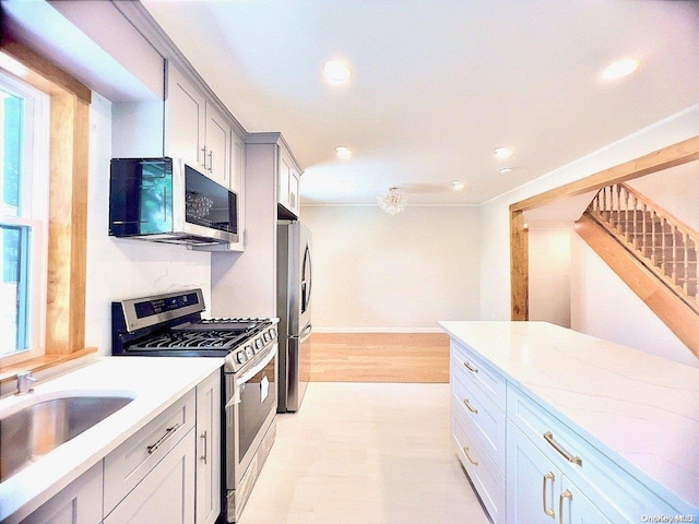 kitchen featuring gray cabinetry, sink, light hardwood / wood-style flooring, light stone countertops, and stainless steel appliances