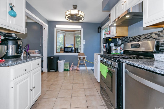 kitchen featuring tasteful backsplash, stainless steel appliances, light tile patterned floors, dark stone countertops, and white cabinets