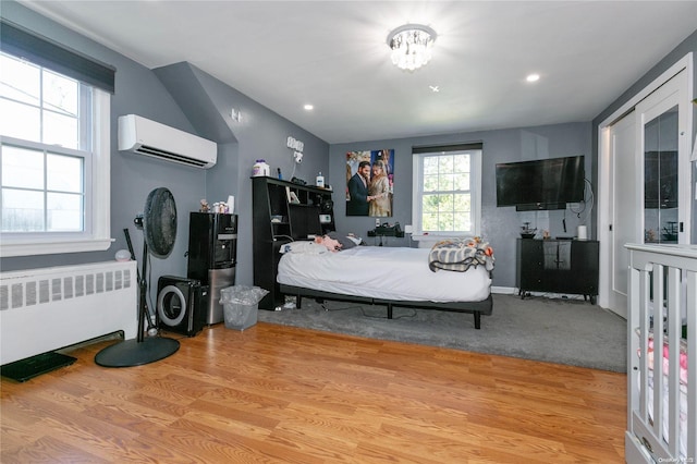 bedroom with an AC wall unit, radiator, and light hardwood / wood-style flooring