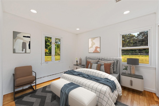 bedroom with light hardwood / wood-style floors and a baseboard heating unit