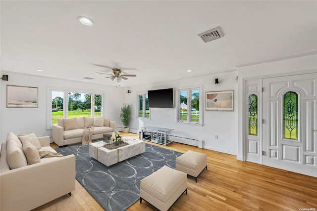 living room with a wealth of natural light, light hardwood / wood-style flooring, and a baseboard heating unit