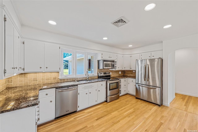 kitchen with appliances with stainless steel finishes, sink, light hardwood / wood-style flooring, dark stone countertops, and white cabinets