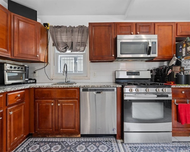 kitchen featuring appliances with stainless steel finishes, tasteful backsplash, light stone counters, sink, and dark tile patterned flooring