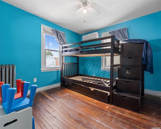 bedroom featuring radiator, hardwood / wood-style flooring, a wall unit AC, and ceiling fan