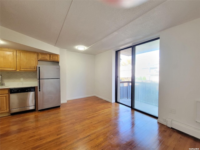 kitchen featuring decorative backsplash, light hardwood / wood-style floors, a textured ceiling, and appliances with stainless steel finishes