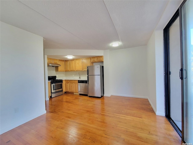 kitchen with appliances with stainless steel finishes, a textured ceiling, light hardwood / wood-style floors, and backsplash