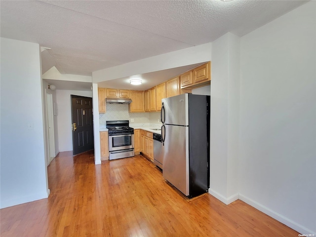 kitchen featuring light wood-type flooring, tasteful backsplash, a textured ceiling, stainless steel appliances, and light brown cabinets