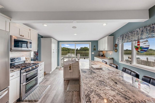 kitchen with light hardwood / wood-style floors, white cabinets, a healthy amount of sunlight, and appliances with stainless steel finishes