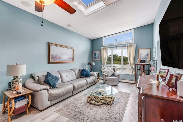 living room featuring vaulted ceiling with skylight, ceiling fan, light hardwood / wood-style flooring, and a baseboard heating unit