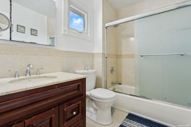 full bathroom with combined bath / shower with glass door, vanity, tile walls, tile patterned flooring, and toilet