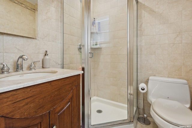 bathroom with vanity, toilet, a shower with shower door, and tile walls