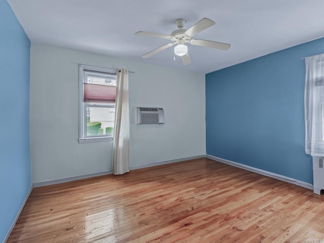 spare room featuring light wood-style flooring, baseboards, a wall mounted air conditioner, and ceiling fan