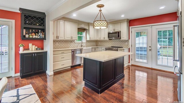 kitchen with dark wood-type flooring, decorative light fixtures, appliances with stainless steel finishes, a kitchen island, and cream cabinetry