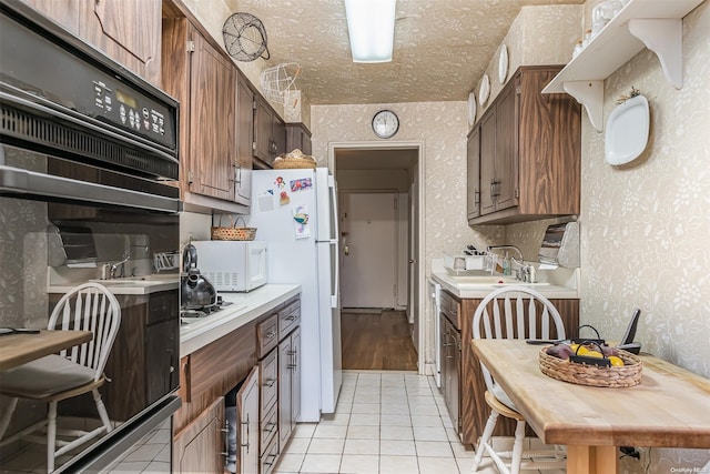 kitchen with a textured ceiling, sink, light tile patterned floors, and white appliances