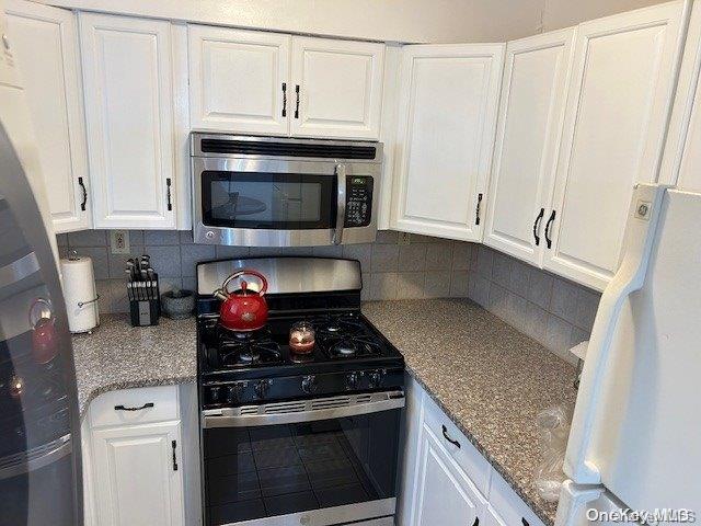 kitchen with decorative backsplash, white cabinetry, stainless steel appliances, and light stone counters