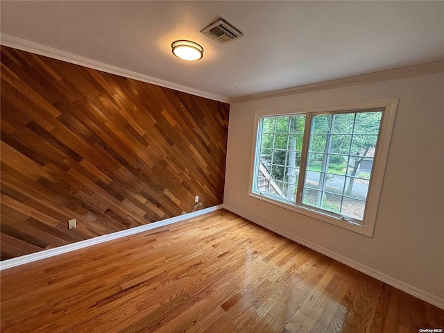 empty room with wooden walls, light hardwood / wood-style floors, and ornamental molding