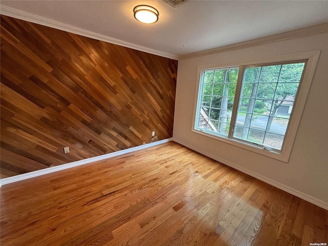 empty room featuring wood walls, ornamental molding, and light wood-type flooring