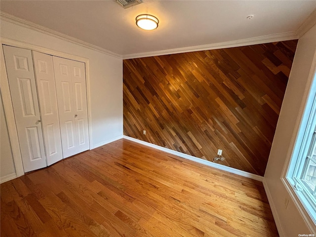 unfurnished bedroom with wood-type flooring, crown molding, wooden walls, and a closet