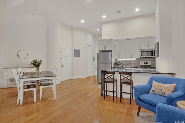 kitchen featuring a kitchen bar, appliances with stainless steel finishes, a towering ceiling, tasteful backsplash, and light hardwood / wood-style floors