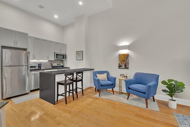 kitchen featuring tasteful backsplash, light hardwood / wood-style floors, a breakfast bar, stainless steel appliances, and gray cabinets