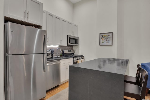 kitchen featuring white cabinetry, sink, light hardwood / wood-style flooring, decorative backsplash, and appliances with stainless steel finishes