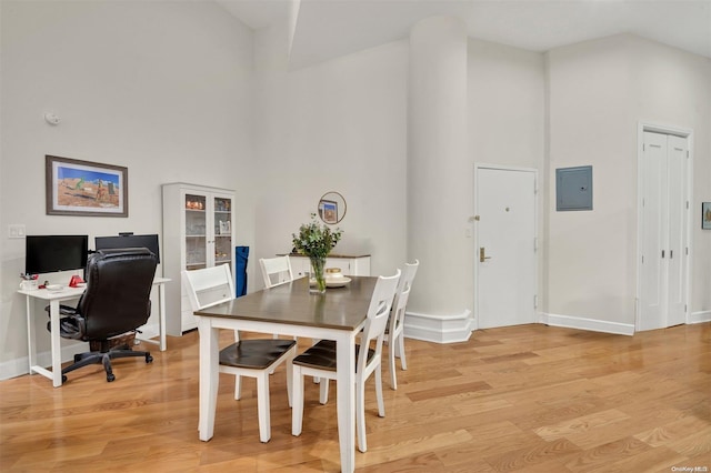 dining area with electric panel, light hardwood / wood-style floors, and a high ceiling