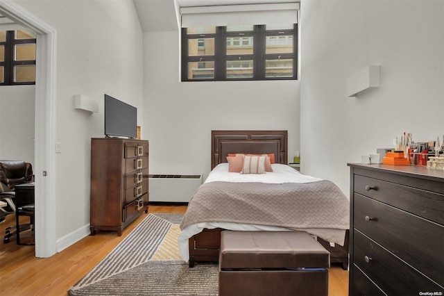 bedroom with light wood-type flooring, a towering ceiling, and a baseboard radiator