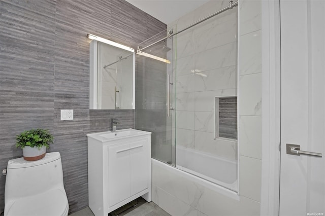 full bathroom with vanity, bath / shower combo with glass door, tile walls, and toilet