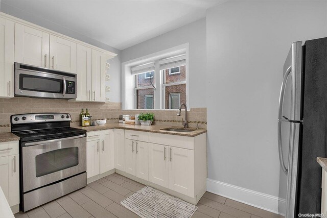 kitchen with decorative backsplash, white cabinetry, sink, and stainless steel appliances