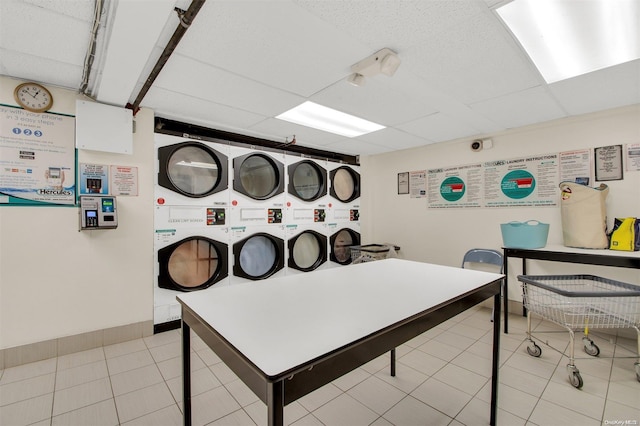 rec room with a drop ceiling, light tile patterned flooring, and stacked washer and clothes dryer