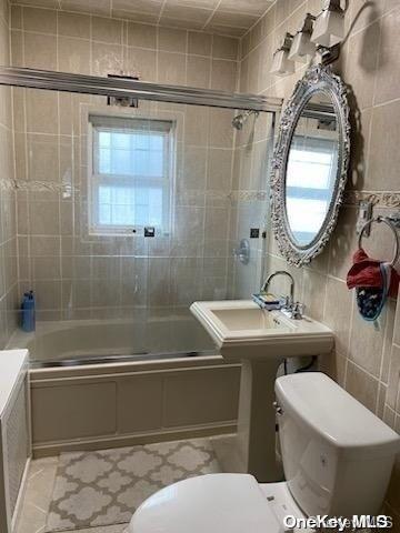 bathroom with combined bath / shower with glass door, tile walls, and a healthy amount of sunlight