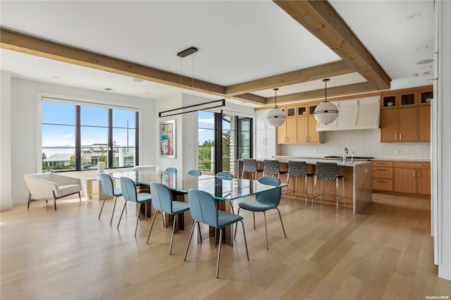 dining area featuring beam ceiling, light hardwood / wood-style floors, and sink