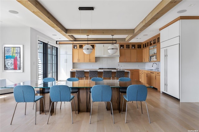 kitchen featuring beam ceiling, sink, backsplash, decorative light fixtures, and light wood-type flooring