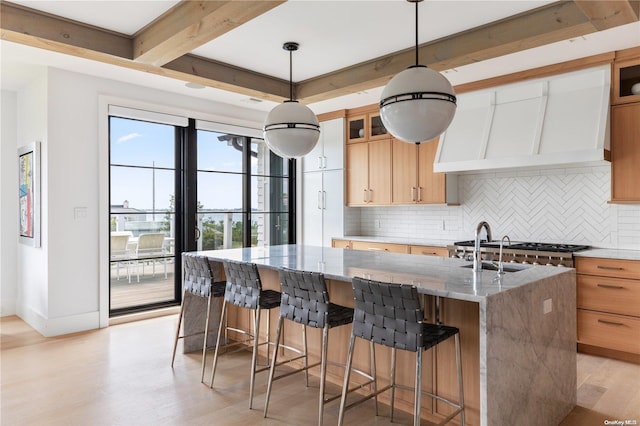 kitchen with pendant lighting, a center island with sink, tasteful backsplash, light hardwood / wood-style floors, and light stone counters