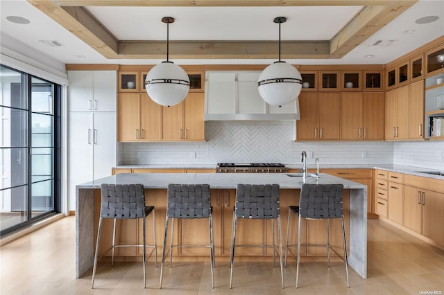 kitchen with light stone countertops, hanging light fixtures, a kitchen island with sink, and a tray ceiling