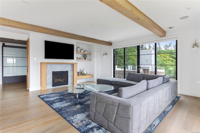 living room with beam ceiling, a high end fireplace, and light wood-type flooring