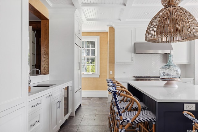 kitchen with white cabinetry, sink, light stone countertops, wall chimney range hood, and a kitchen island